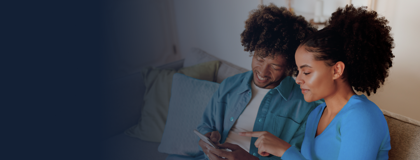 Casal jovem sentado no sofá olhando juntos para a tela de um smartphone.