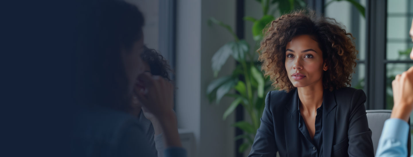 Mulher de cabelos cacheados e blazer escuro em reunião de negócios em escritório moderno.