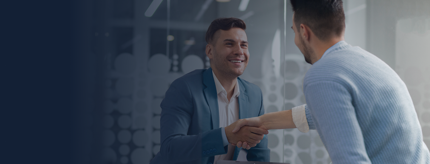 Dois homens se cumprimentando com aperto de mão em escritório moderno com divisórias de vidro.