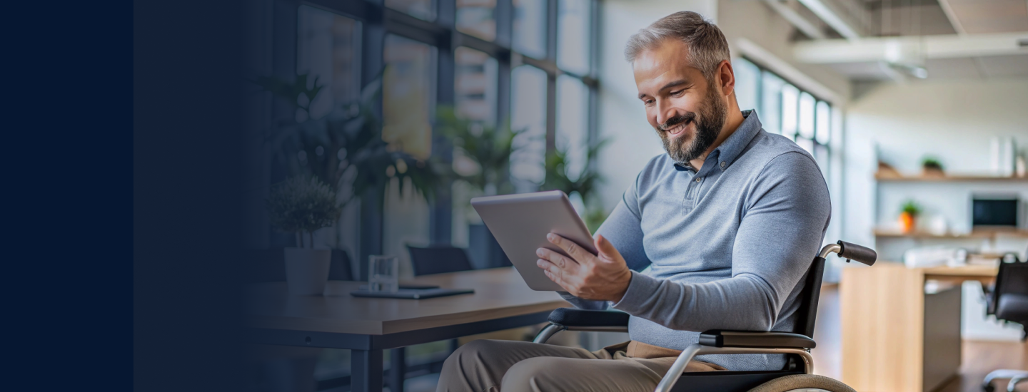Homem adulto em cadeira de rodas sorrindo enquanto usa um tablet em escritório moderno e iluminado.