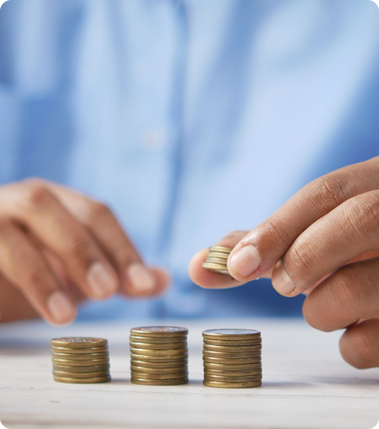 Mãos de pessoa empilhando moedas sobre uma superfície clara, com três pilhas de alturas crescentes