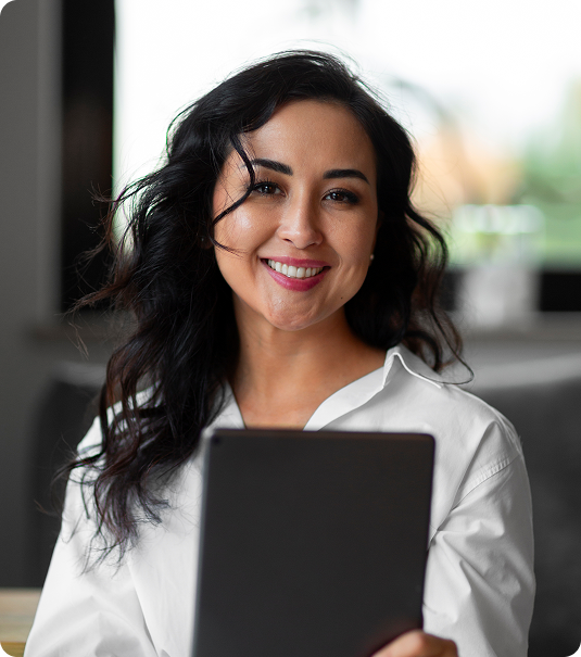 Mulher adulta de cabelos escuros sorrindo enquanto segura um tablet em ambiente interno.