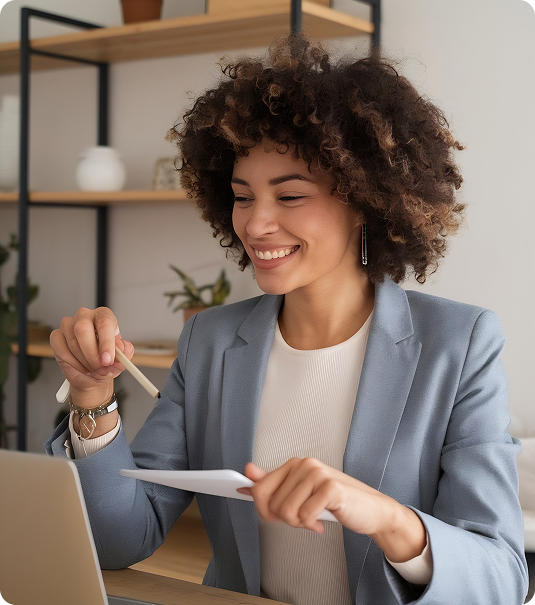 Mulher jovem de cabelos cacheados e blazer azul sorrindo enquanto analisa um documento em frente ao laptop.