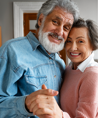 Casal de idosos sorrindo e se abraçando em ambiente doméstico.