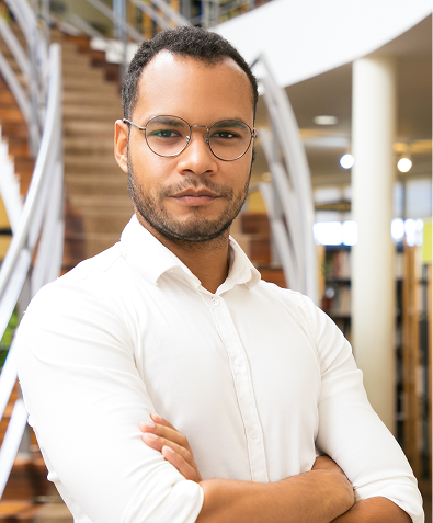 Homem jovem de óculos e camisa branca com os braços cruzados, em ambiente interno.
