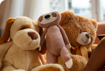 Três pelúcias enfileiradas: um cachorro, uma preguiça e um urso marrom.