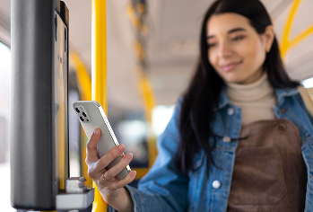 Mulher jovem aproximando o smartphone de um terminal de pagamento dentro de um ônibus
