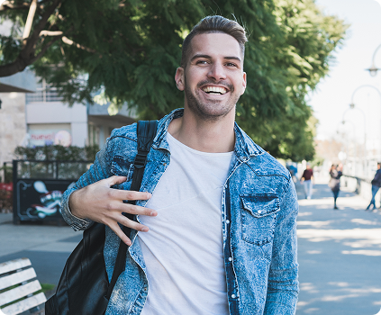 Homem sorridente com mochila no ombro, vestindo camisa Jeans e camiseta branca